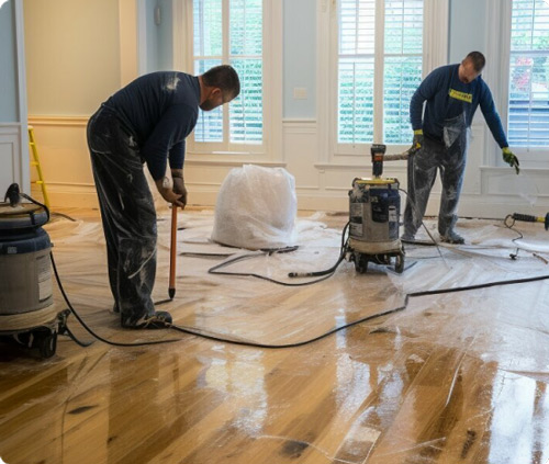 Environmental remediation contractors restoring a hardwood floor in a residential space, using specialized equipment for safe and thorough cleanup