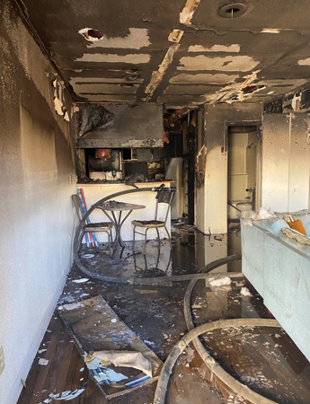 Fire damage in an apartment with a deployed fire hose, showcasing charred walls and water from firefighting efforts.